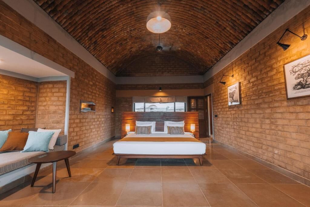 A spacious room with a large bed, a seating area with a sofa and a small table, brick walls, and a wooden ceiling.