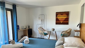 A bedroom with a bed, two wicker chairs, a small table, a wall-mounted lamp, and a painting. - Chambre La Centrale : private terrace -Heated swimming pool, 5mn from the beach (Soorts-Hossegor)