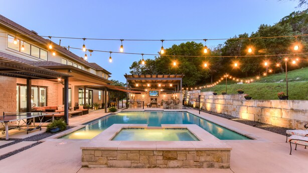 A pool area with lounge chairs, string lights, and a stone wall.