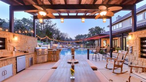 An outdoor pool area with a stone barbecue, seating, and string lights.