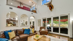 A spacious living area with a brown leather sofa, a wooden coffee table, and a large window with a view of a green landscape.