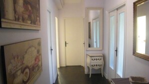 Ein Flur mit einer weißen Tür am Ende, einer kleinen, weißen Kommode mit Schubladen und einem Spiegel darüber.