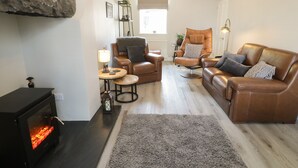 A cozy living room with a fireplace, leather sofas, a round coffee table, and a stone accent wall. - Minffordd (Blaenau Ffestiniog)