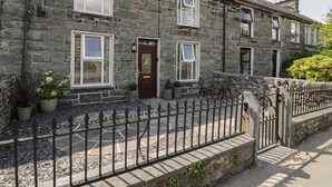 A stone house with a dark brown door, white-framed windows, and a metal fence. - Minffordd (Blaenau Ffestiniog)