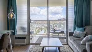 A modern living room with a large sliding glass door leading to a balcony, a sofa, a coffee table, and a desk with a chair.