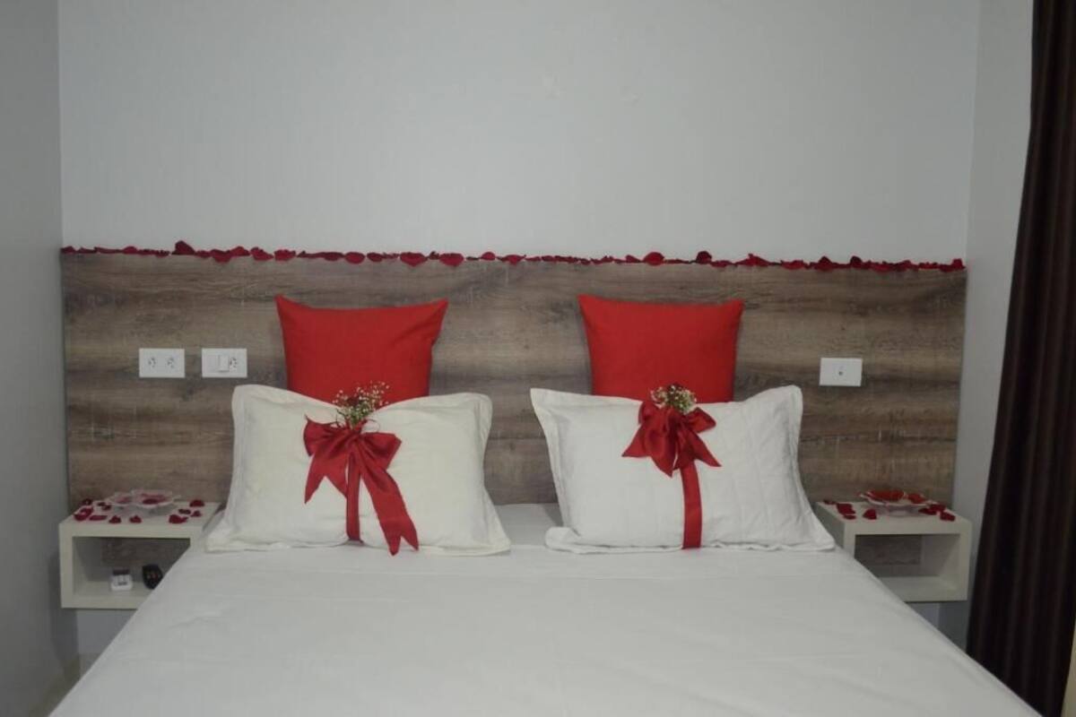 A double bed with white linens and red pillows, a wooden headboard, and bedside tables with red rose decorations.