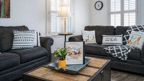 Un salon avec deux canapés en cuir foncé, une table basse en bois, une plante en pot et un panneau d’accueil encadré.