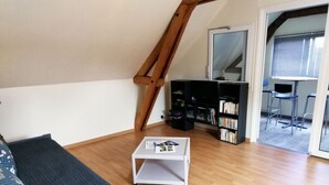 A cozy loft-style room with a wooden floor, a gray sofa, a white coffee table, and a bookshelf. - Spacious accommodation surrounded by greenery (Mouliherne)