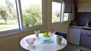 A kitchen with a round table, chairs, a refrigerator, and a window with a view of greenery. - Spacious accommodation surrounded by greenery (Mouliherne)
