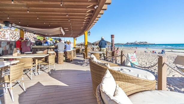 Een strandbar met rieten meubels en een houten terras, met uitzicht op het strand en de oceaan.