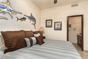 A bedroom with a large bed, striped bedding, a nightstand with a lamp, and wall art including shark and framed pictures.