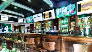 Een bar met meerdere schermen waarop sportbeelden te zien zijn, diverse drankflessen en klassieke barstoelen.