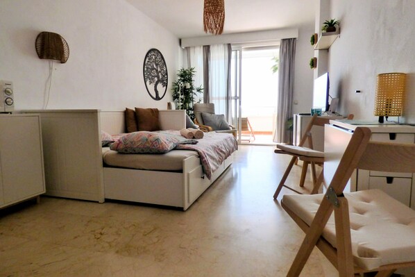 A modern living room with a sofa, a dining area with a table and chairs, a large window with a view, and a wall-mounted plant shelf.