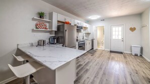 A modern kitchen with white cabinetry, a marble countertop, and a wooden floor.