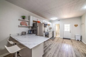 Une cuisine moderne avec des meubles blancs, un plan de travail en marbre et un plancher en bois.