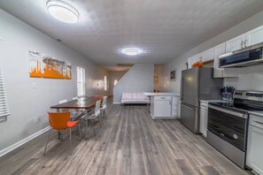 A modern kitchen with white cabinets, stainless steel appliances, and a dining area with a wooden table and chairs. - Orange Crush Townhome I, Beach & Pet-Friendly (Cape Charles)