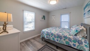 A bedroom with a bed, a nightstand, a lamp, and two windows with blinds.