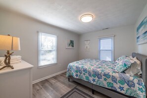 A bedroom with a bed, a nightstand, a lamp, and two windows with blinds. - Orange Crush Townhome I, Beach & Pet-Friendly (Cape Charles)