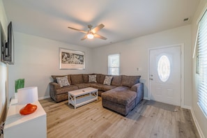 A living room with a sectional sofa, a coffee table, a ceiling fan, and a door with a frosted glass window.