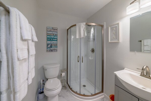 A bathroom with a glass-enclosed shower, a toilet, a sink, and a towel rack.