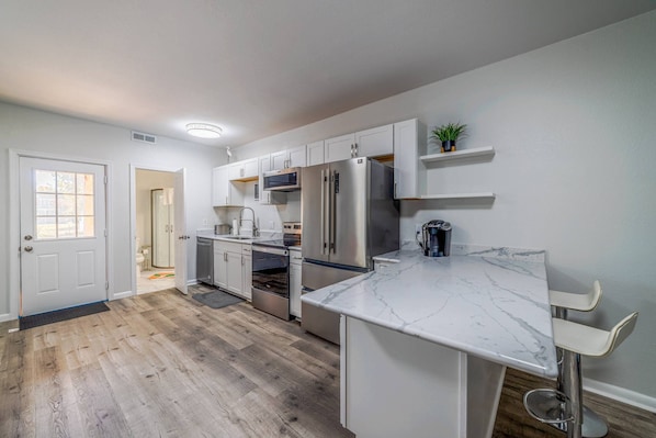 Una cocina moderna con armarios blancos, encimera de mármol y electrodomésticos de acero inoxidable.