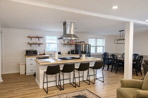 A modern kitchen with a central island, bar stools, and a dining area with chairs. - Delightful Cottage•Pet Friendly•Fenced Yard (Rehoboth Beach)