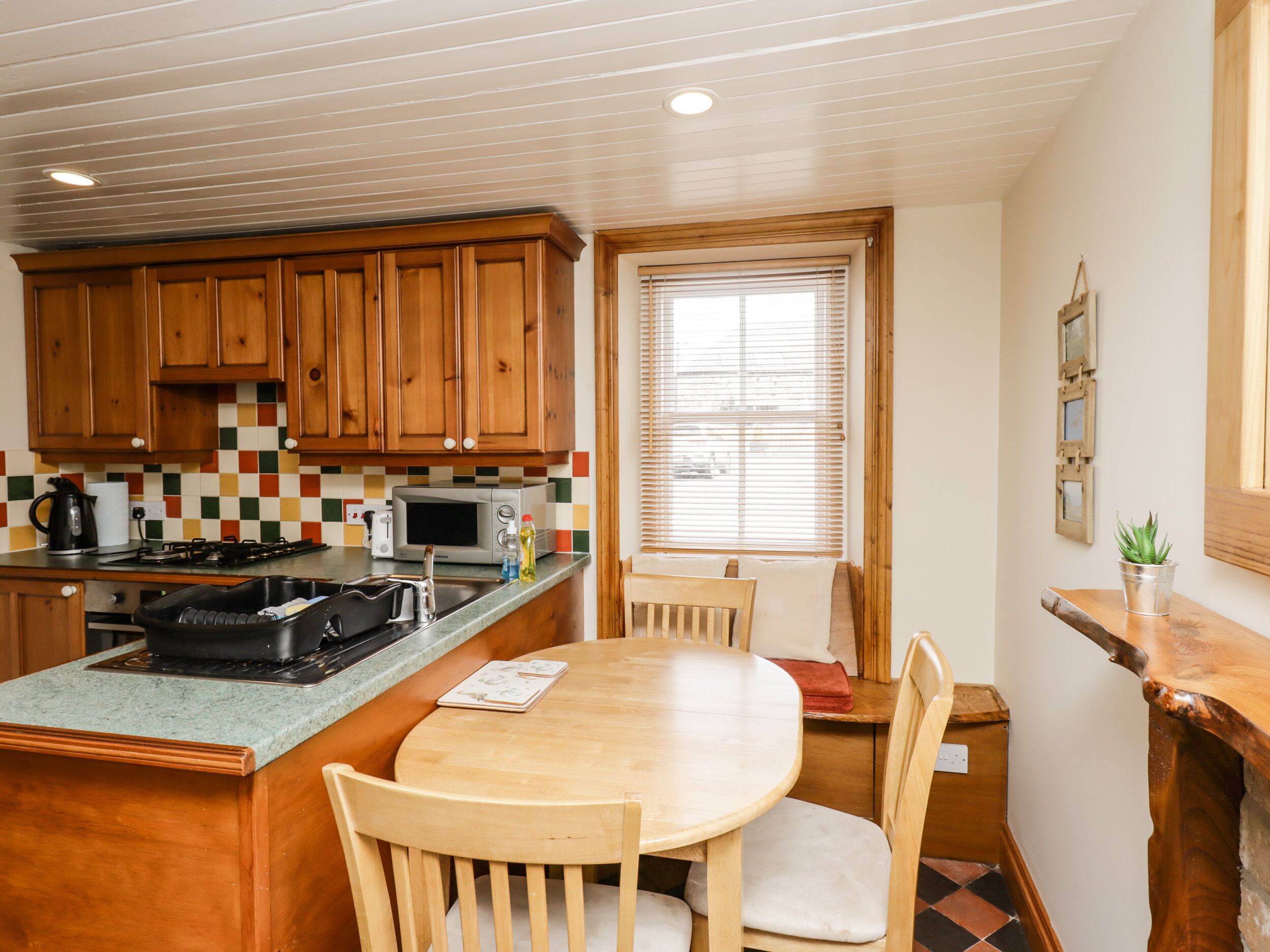 A compact kitchen with wooden cabinets, a microwave, and a dining area with a wooden table and chairs.