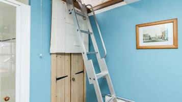 A room with a blue wall, a wooden door, a white radiator, and a ladder leaning against the wall.