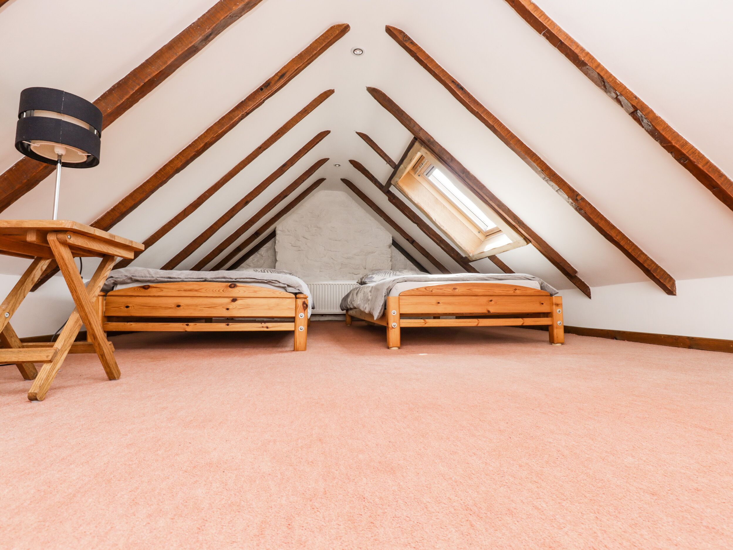 Ein kleines Schlafzimmer im Dachgeschoss mit zwei Holzbetten, einem Schreibtisch und einer Lampe.
