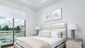 Habitación de hotel moderna con una cama grande, dos mesitas de noche con lámparas, vista de la ciudad desde un balcón y dos obras de arte enmarcadas.