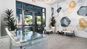 Un vestíbulo moderno con una mesa de cristal, dos sillones blancos y una pared de mármol.