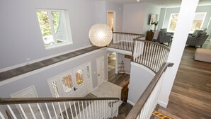 En interiör med flera nivåer, ett trätrapphus, en hängande lampa och utsikt över ett vardagsrum med möbler.