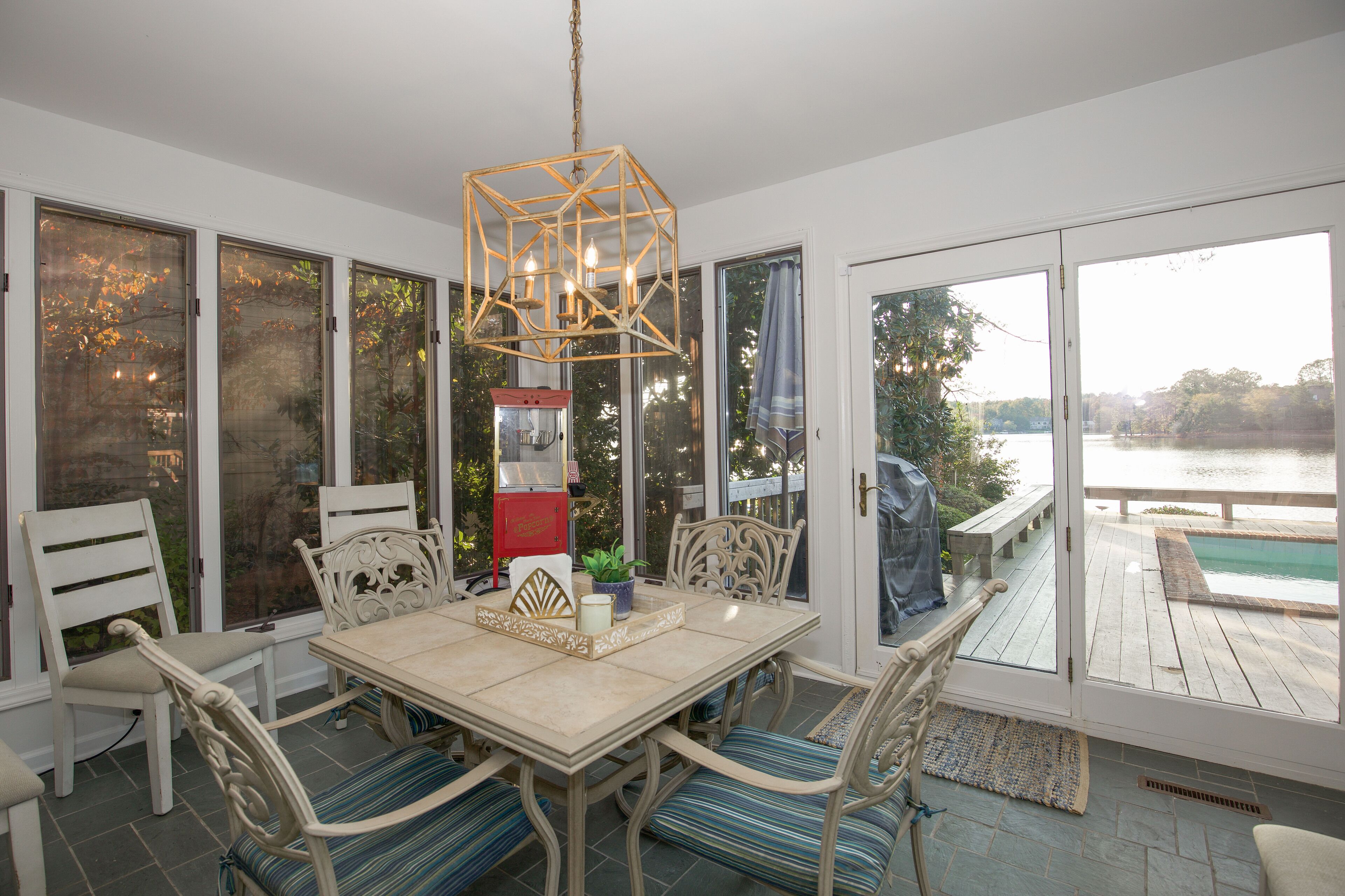 A dining area with a table and chairs, a hanging light fixture, and large windows with a view of a body of water.