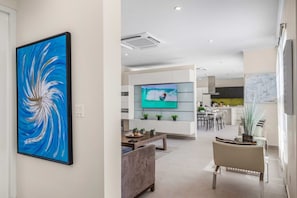 A modern living room with a flat-screen TV, a sofa, and a dining area with a table and chairs.