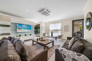 A modern living room with a flat-screen TV, a coffee table, and a sofa. - Villa Haven: 6BR w/ Private Pool Near Palm Beach! (Noord)