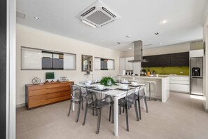 A modern kitchen with a dining area, featuring a central island, a built-in oven, and a stainless steel refrigerator. - Villa Haven: 6BR w/ Private Pool Near Palm Beach! (Noord)