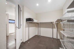 A corner room with a white door, a shelf with a black object, and metal wire shelves.