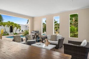A modern living room with a pool view, wicker furniture, and a barbecue area.