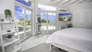 A bedroom with a large bed, a vanity, a TV, and a balcony with a view of the ocean. - Oceanfront 2 Homes | Private Beach & Pool | 3 Acre (Islamorada)