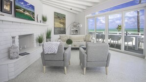 Una sala de estar moderna con chimenea, sillones grises y un ventanal con vistas al océano.