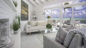 Una sala de estar moderna con un sofá blanco, una mesa de centro de cristal y vistas al océano a través de grandes ventanales.