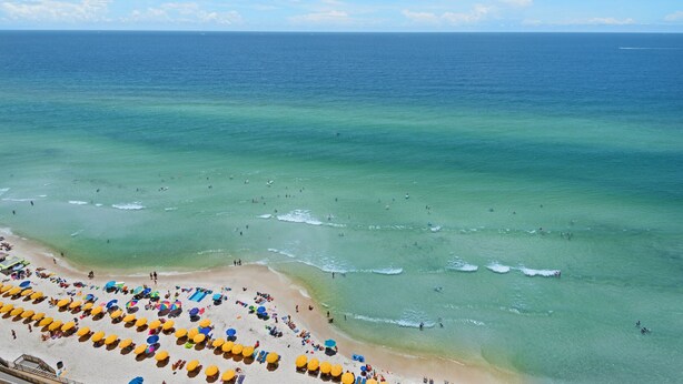 Ein Strand mit klarem türkisblauem Wasser, einem sandigen Ufer und zahlreichen Sonnenschirmen.