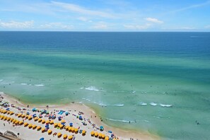 Une plage à l’eau turquoise et limpide, avec un rivage sablonneux et de nombreux parasols.