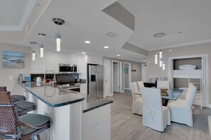 Une cuisine moderne avec des armoires blanches, un comptoir en granit et des appareils en acier inoxydable. On y trouve un coin repas avec des chaises blanches et une table en verre.