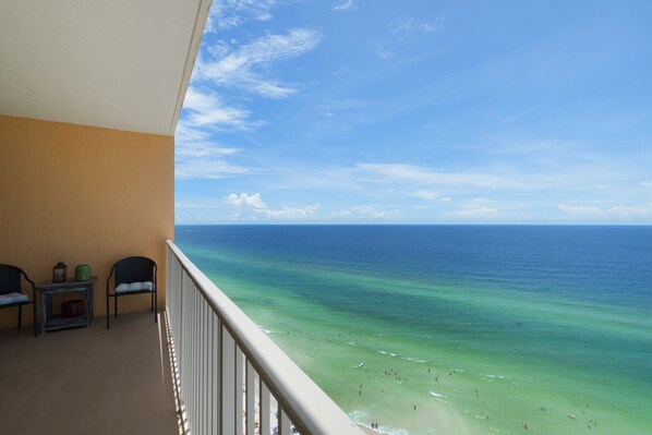 A balcony with a view of the ocean, two chairs, and a small table with a lantern and a green mug.