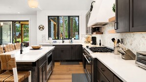 A modern kitchen with dark cabinetry, a central island, and a large window providing a view of the outdoors.