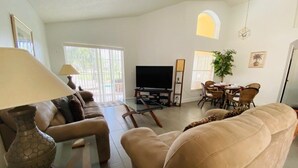 Una sala de estar con sofá, mesa de centro de vidrio, televisor y un comedor con sillas y mesa.