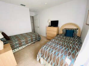 A bedroom with two beds, a dresser, a television, and a door.