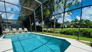 Una piscina con agua azul cristalina, rodeada por una zona cubierta con sillas y vistas a árboles y una casa al fondo.