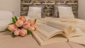 Ein ordentlich bezogenes Bett mit weißen Leinentüchern, ein Strauß rosa Tulpen und ein offenes Buch mit herzförmigen Seiten auf einer beigen Tagesdecke.